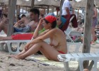 Dark haired chick with a red kerchief sitting topless under the parasol