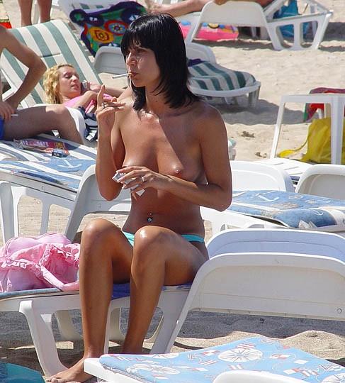 Sexy brunette girl smoking a cigar on the beach while a pervert poses her beautiful big boobs