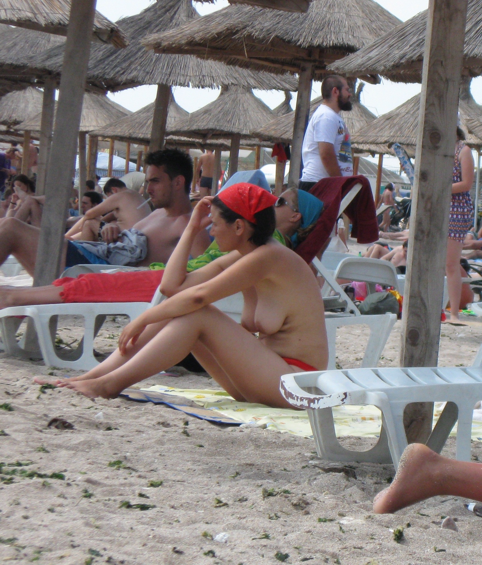 Dark haired chick with a red kerchief sitting topless under the parasol
